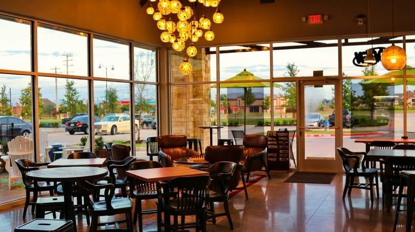 Warmly lit restaurant interior with diverse seating, large windows, and a view of a parking lot.
