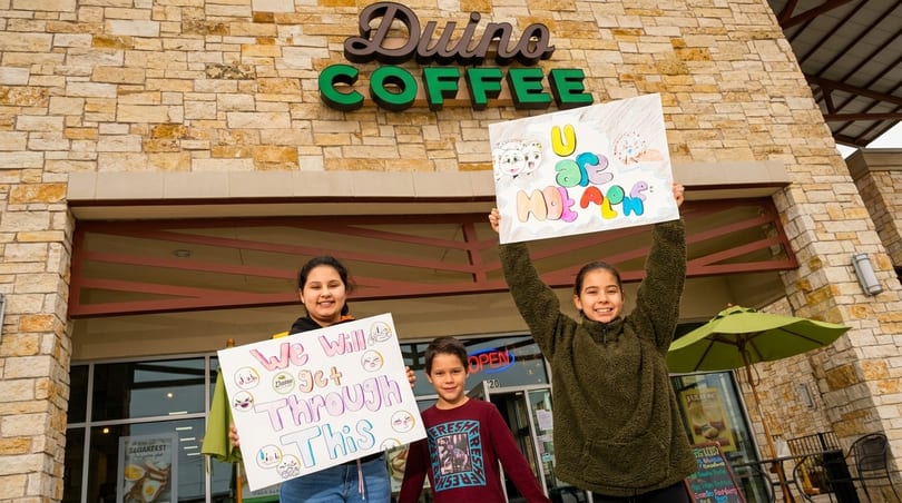 Three children holding handmade signs in front of a Duino Coffee shop entrance.
