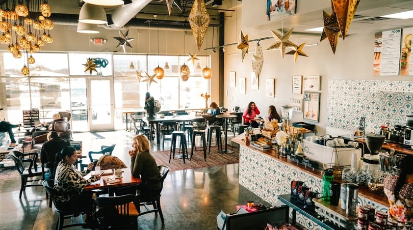 A bright, spacious coffee shop with customers seated at tables and a patterned counter.