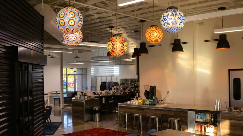 Colorful mosaic globe lights illuminate a modern cafe with a long counter and bar stools.